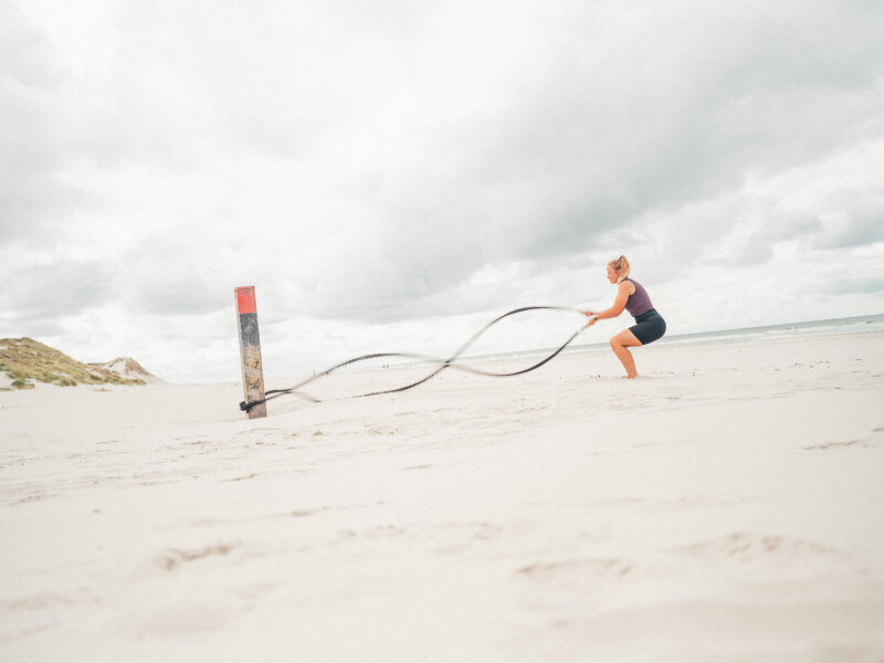 Vrouw die een bootcamp oefening doet op het strand.