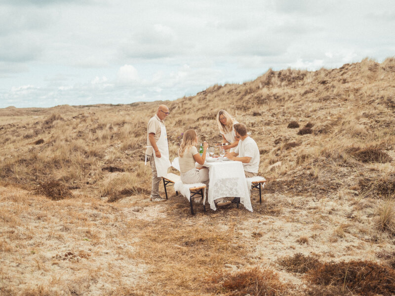 2 lokale ondernemers die uitleg geven over het eten aan een stel dat dineert tussen de duinen.