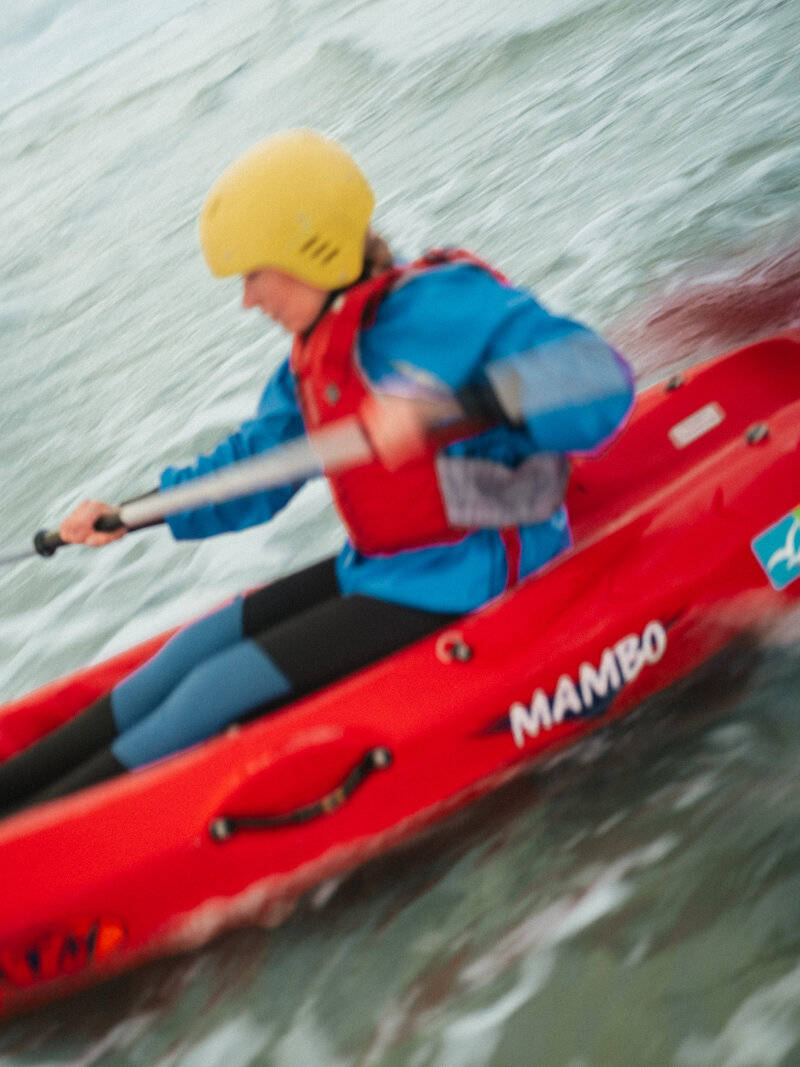 Vrouw met gele helm in rode kayak in de zee van Terschelling.