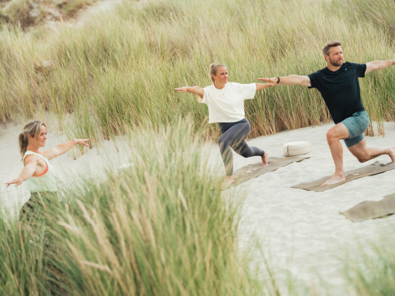 Drie mensen doen yoga tussen de duinen van Terschelling.