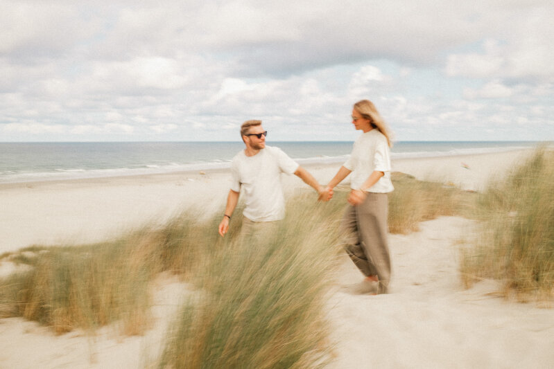 stel dat hand in hand tussen de duinen loopt met uitzicht op zee.